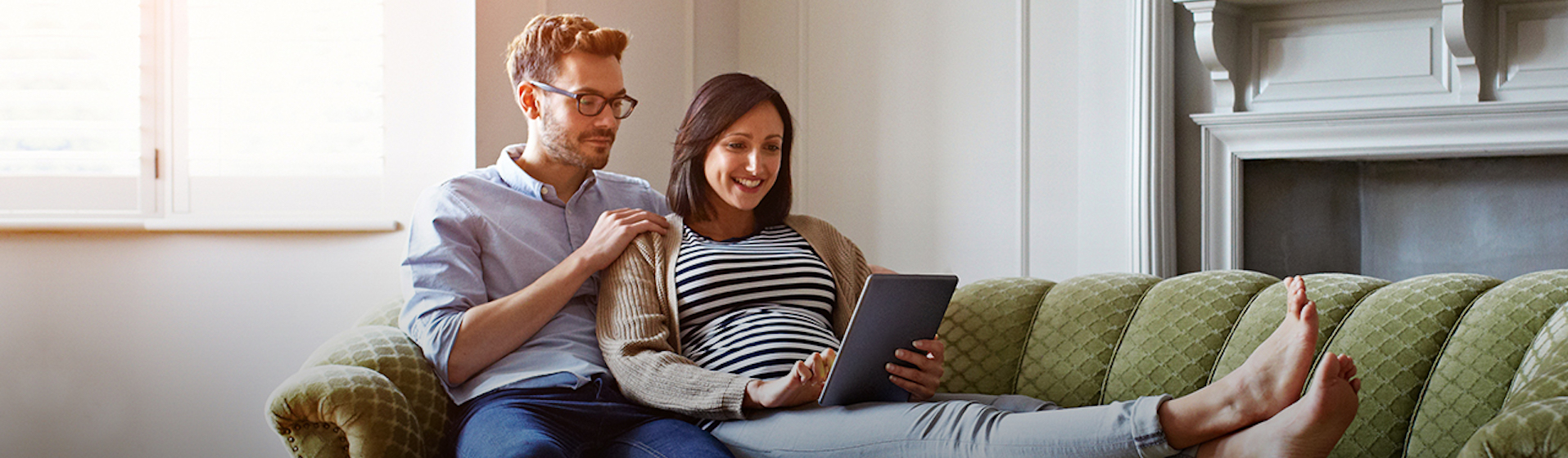 Pregnant woman and man sitting on couch looking at tablet